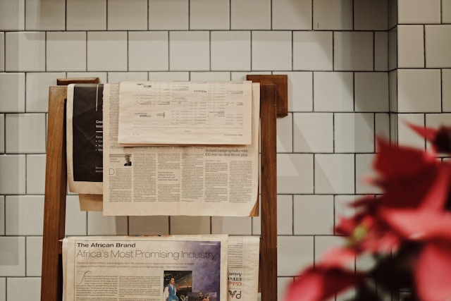 A white tiled wall with an attached rack containing folded newspapers.