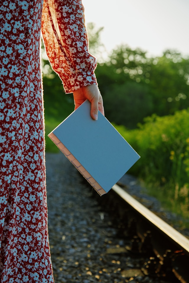 Side view of a figure in a red and white dress holding a blue book in their hand. 